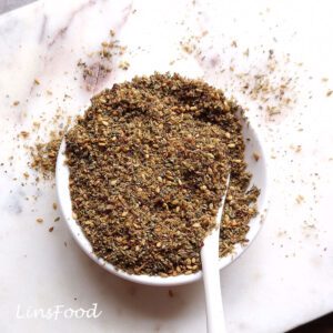 Bowl of homemade za’atar spice mix with sesame seeds, sumac and dried herbs, with a white spoon.