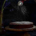 Sprinkling sugar on torta caprese, chocolate cake, dark photo