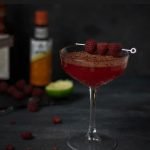 Raspberry margarita with chocolate sprinkle and raspberries on coktail stick