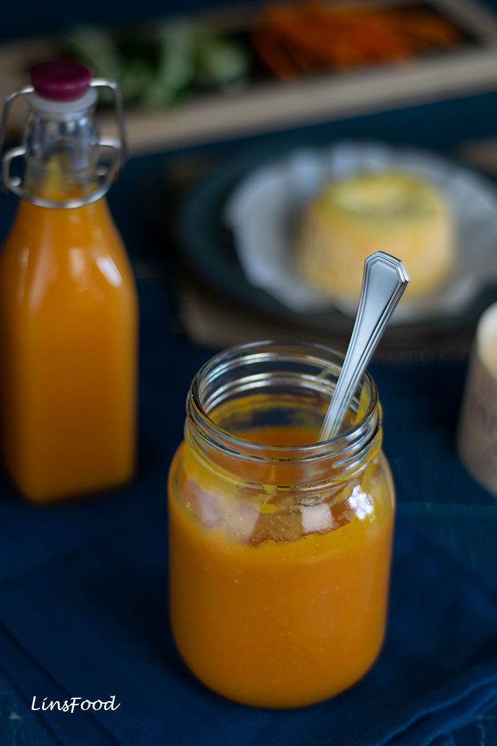 orange coloured hot sauce in glass jar with bottle in the background