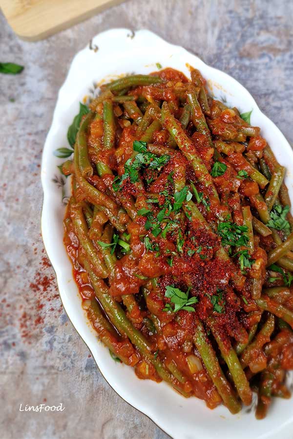 Three-quarter angle of vegan fasolia bi zeit served in a patterned oval china dish, topped with parsley and Aleppo flakes.