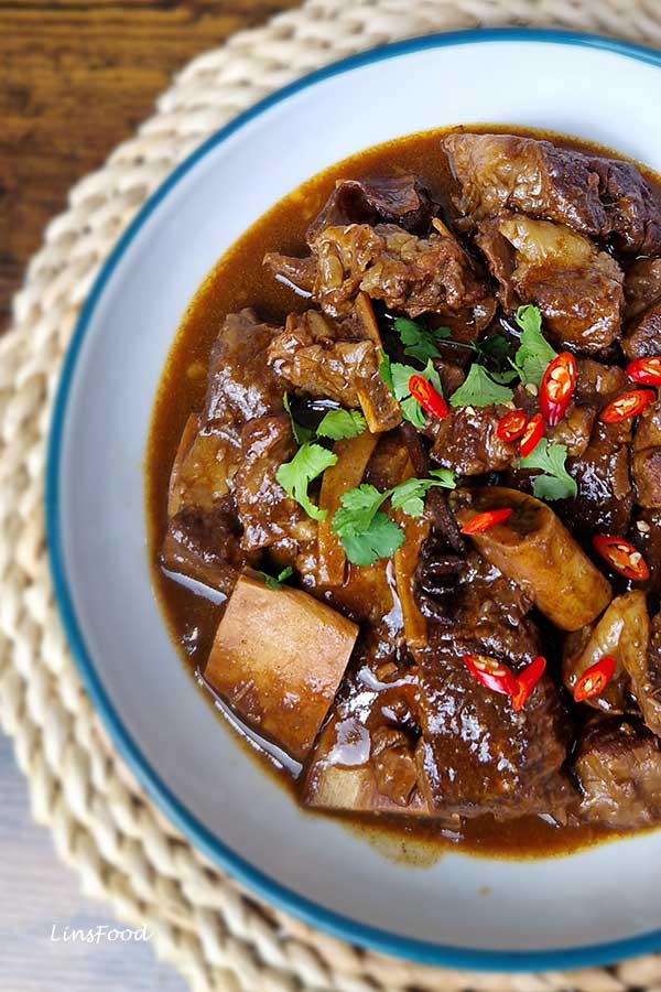 Close-up top shot of Chinese braised beef short ribs with lacquered sauce, red chilli slices and coriander in a light bowl.