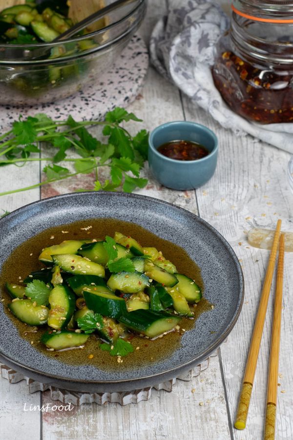 Chinese smashed cucumber salad on a dark plate with chopstics and chilli oil
