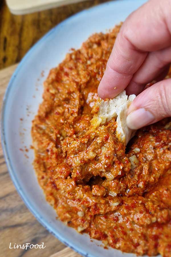 Hand scooping muhammara roasted red pepper and walnut dip with a piece of flatbread.