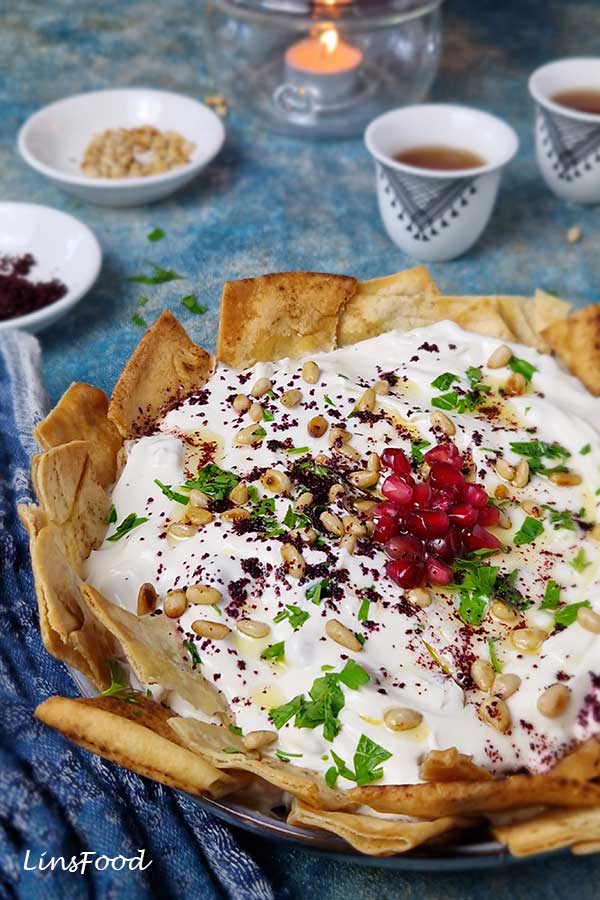 Close view of chickpea fatteh with crispy pita, yoghurt, pine nuts, parsley and pomegranate seeds