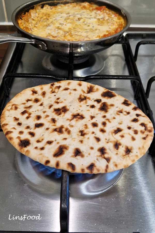Flatbread being heated over a gas flame to serve with Yemeni lahsa.