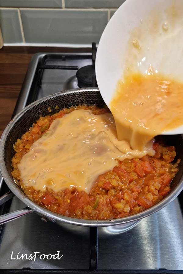 Beaten eggs being poured into the cooked tomato and onion base for Yemeni lahsa.