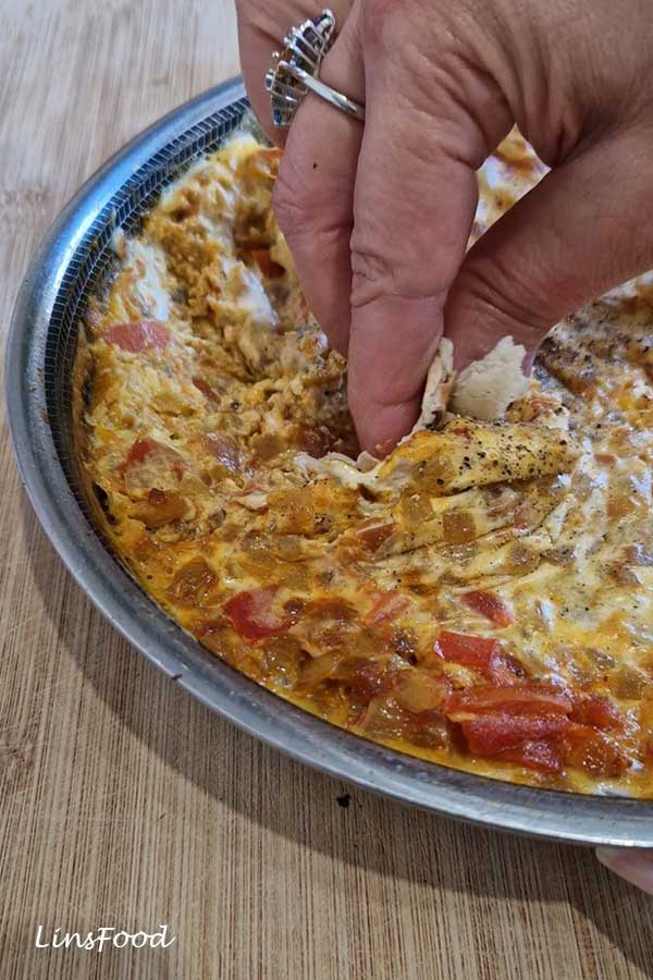 A hand scooping creamy Yemeni lahsa with a piece of flatbread from the pan.