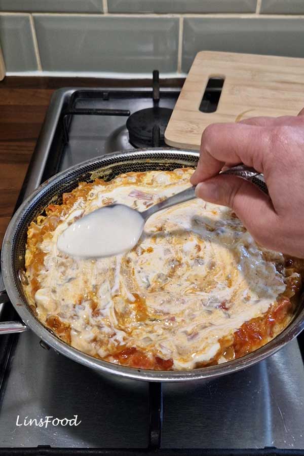 Creamy cheese being spread over cooked Yemeni lahsa in a pan.