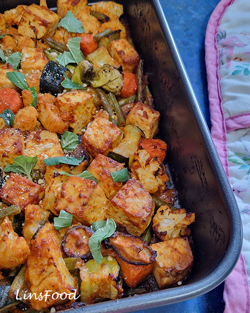 Close-up of red Thai curry tofu and veg traybake with herbs and roasted vegetables.