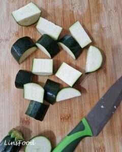 Chopped courgette pieces on a wooden board for red Thai curry tofu and veg traybake.