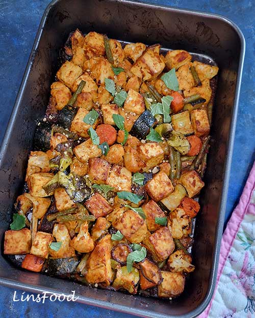 Red Thai curry tofu and vegetable traybake in a roasting tin with herbs scattered on top.