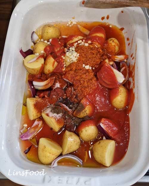 Potatoes, red onion and garlic with passata, sundried tomato paste, olive oil and spices for vegan fasolia traybake.
