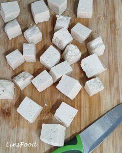 Cubes of extra-firm tofu on a wooden chopping board.