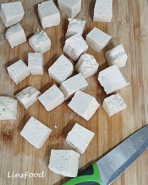 Cubes of extra-firm tofu on a wooden chopping board.