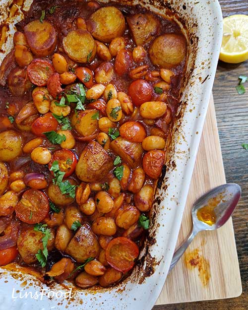 Close-up of vegan fasolia traybake with creamy butter beans, potatoes and tomatoes in a thick tomato sauce.