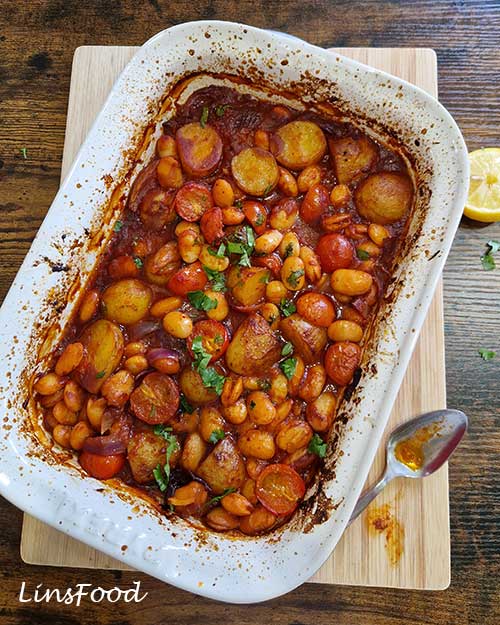 Overhead shot of vegan fasolia traybake with butter beans, potatoes, cherry tomatoes and parsley.