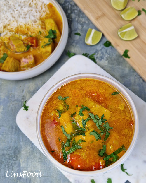 An overhead photograph of golden Omani paplou with chunks of fresh tuna, softened tomatoes and chopped coriander, with basmati rice and lime wedges in the background.