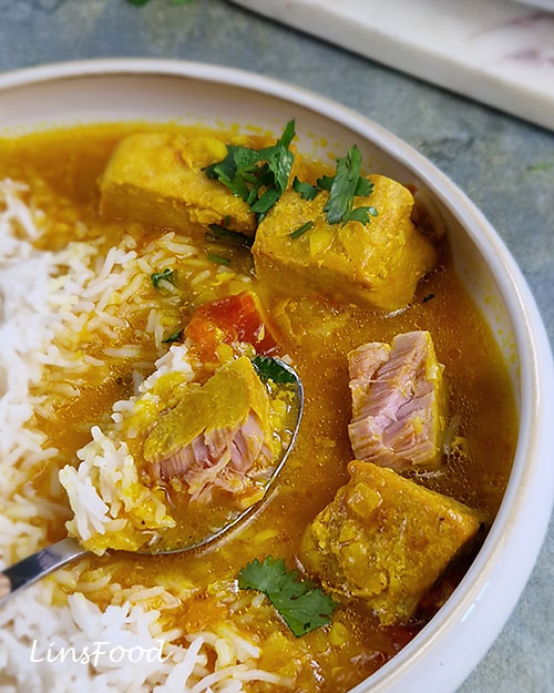 Omani paplou served with plain basmati rice, with a spoonful showing a tender piece of tuna, rice and golden lime and turmeric broth, in a white bowl.