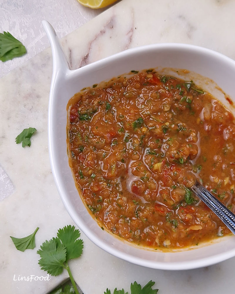 White bowl of daqqus with a spoon, coriander leaves and lemon